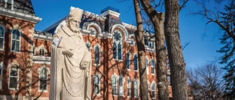 A stone statue of Saint Ambrose of Milan outside in the snow.